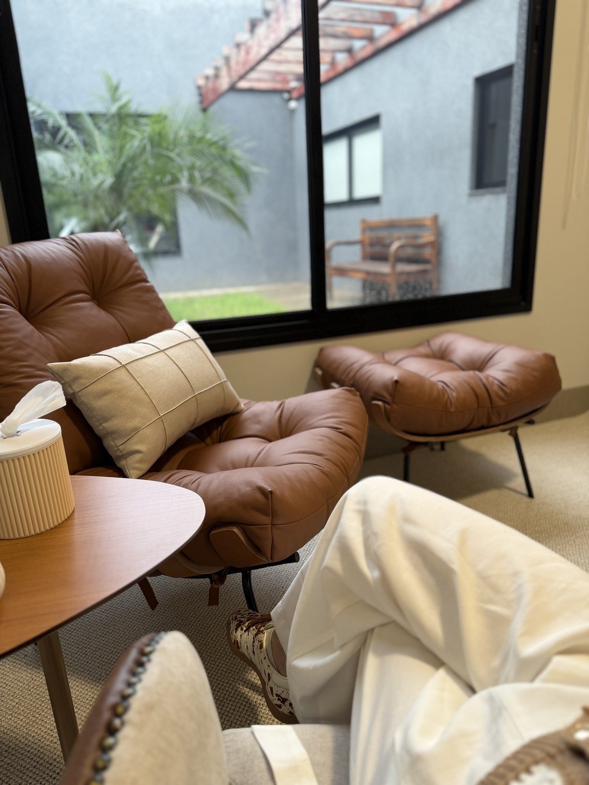 Consultório em Araçatuba: poltronas de couro caramelo, mesa lateral e janela com vista para área verde